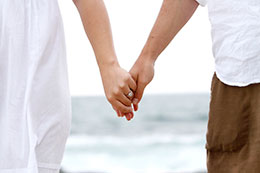 Engaged couple hold hands with beach in the back
