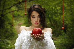 Beautiful girl is Snow White looking at red apple in foreground