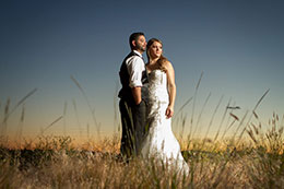 Bride and Groom stand in a field during sunset