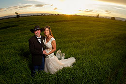 Newly married couple stands in field at sunset
