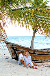 Couple snuggles beside an old boat and a palm tree