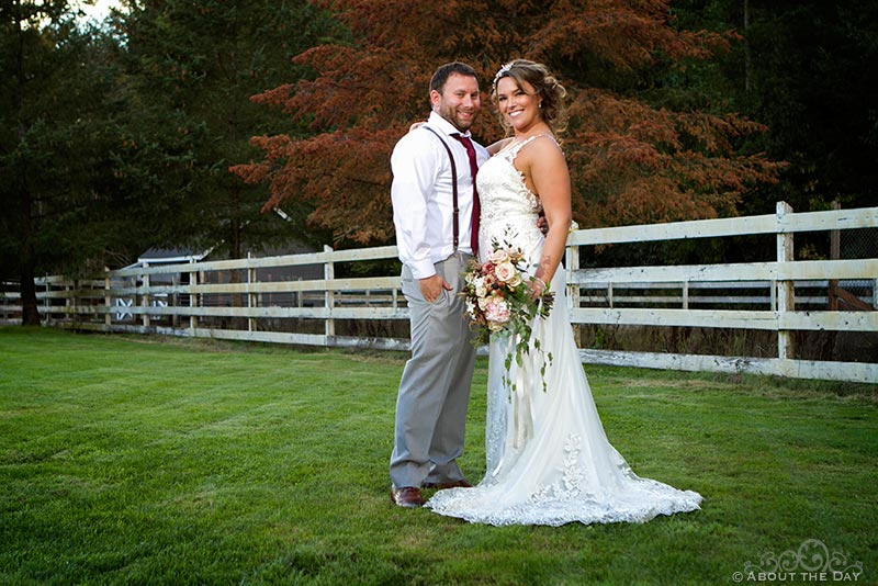 Bride and Groom pose in the field with a white fence