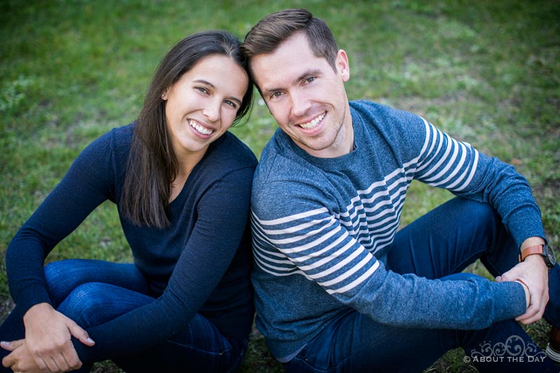 Engaged couple sit back to back on the grass