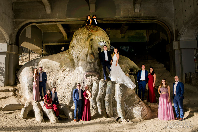 Andrew and Alex and their wedding party stand all over the Fremont Troll