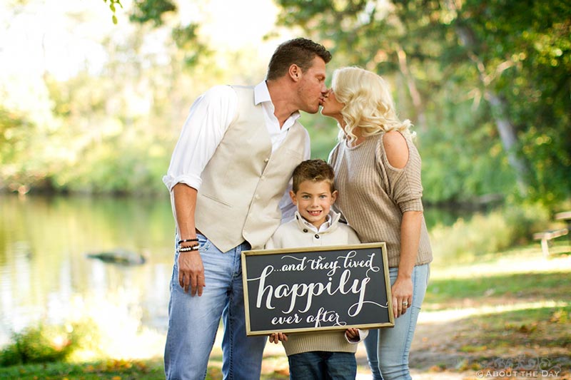 Engaged couple kiss with their son holding a sign at Rock Cut State Park