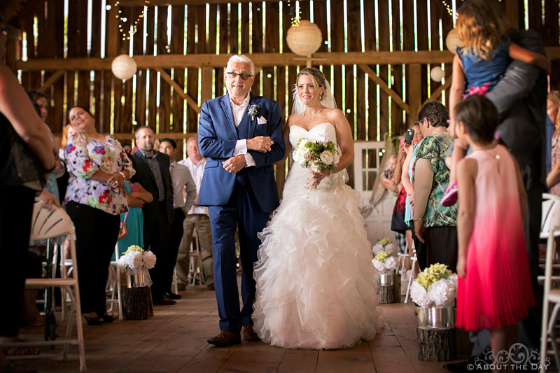 Bride and her father walk down the isle in the barn at Youngs Dairy Farm in Auburndale, WI