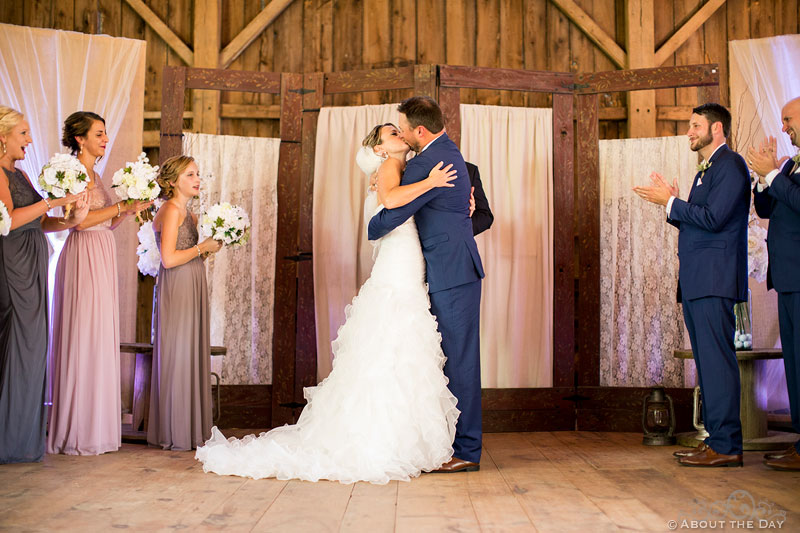 Cody and Bridget kiss during wedding in the barn at Youngs Dairy Farm in Auburndale, WI