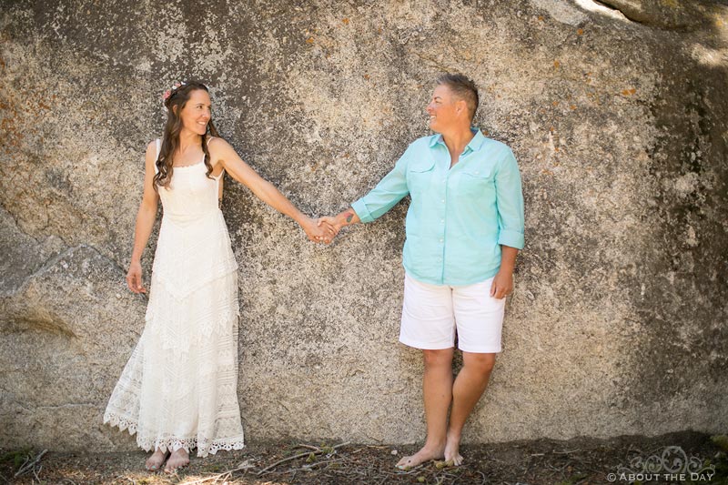 Brides hold hands and lean against a rock wall