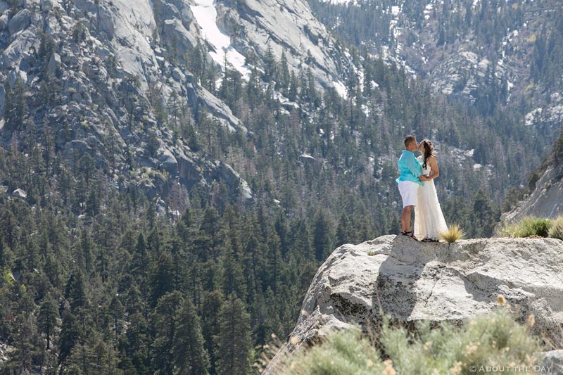 Brides kiss on a rock high above the valley