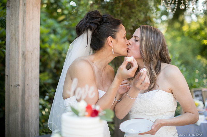 Brides kiss with wedding cake at Albees Garden in Olympia