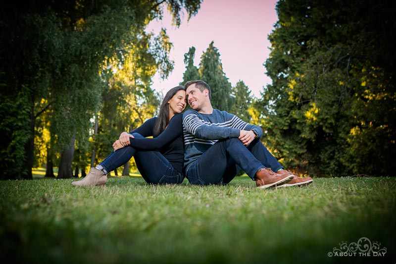 Engaged couple sit back to back on the grass at Greenlake