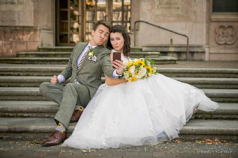 The Bride and Groom do a selfie sitting on the steps of Gerberding Hall