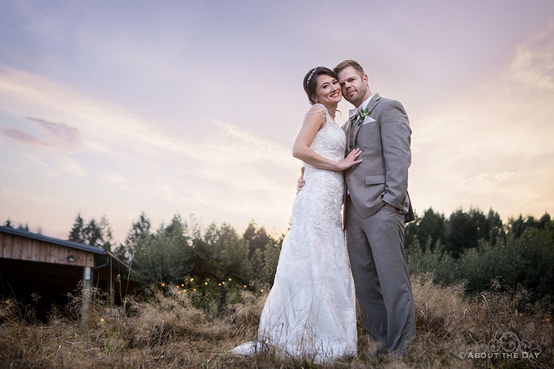 The Bride and Groom standing tall during sunset with The Orchard at Sunshine Hill in the background