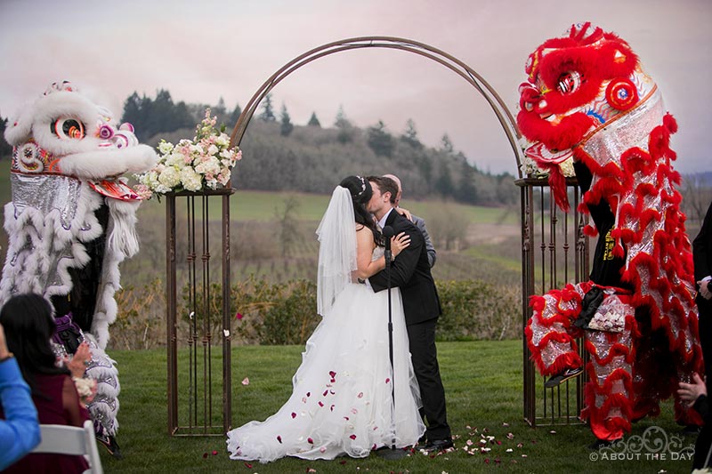 Bride and Groom kiss during ceremony with Chinese lions at Zenith Vineyards